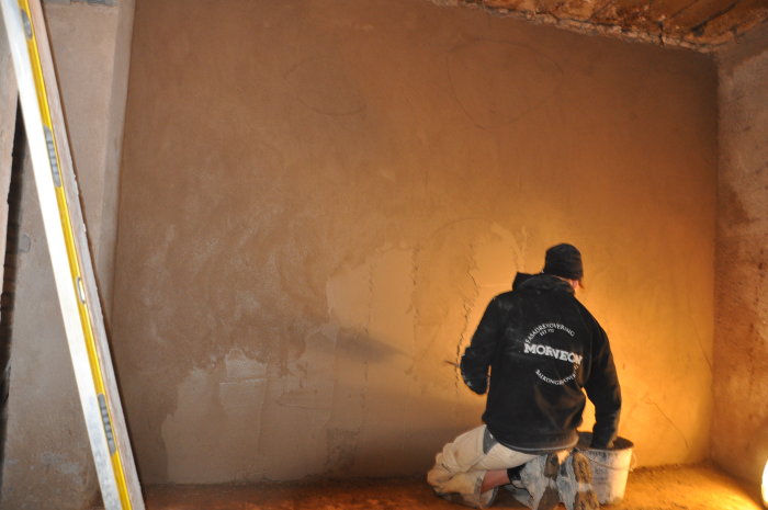 Person i arbetskläder applicerar kalkbruk på en vägg med hjälp av en slev.