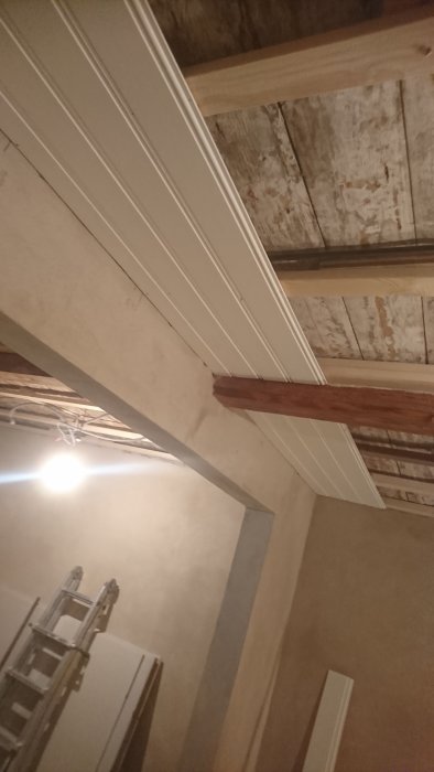 Renoverat vardagsrum med nyputsade väggar, oljad bjälke och påbörjad taklattning.