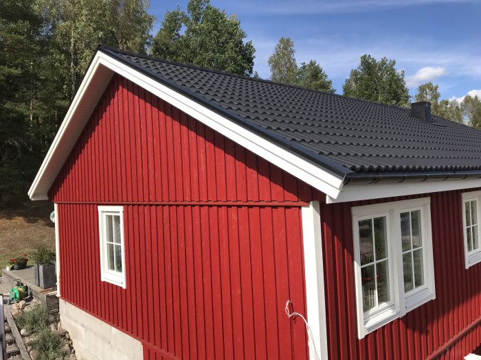 Renoverat hus med rött träfasad och nytt svart tak.