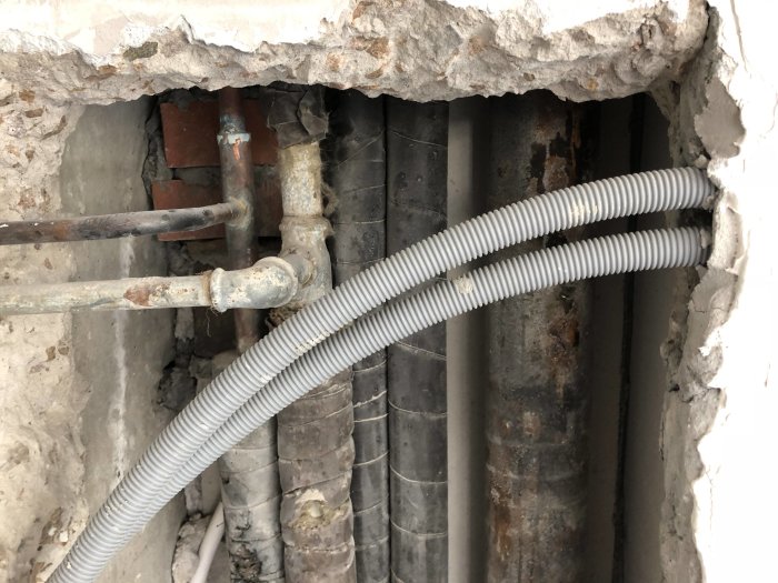 Öppet schakt med synliga rör inklusive galvaniserat vattenrör och gjutjärnsavloppsrör för renovering i kök.