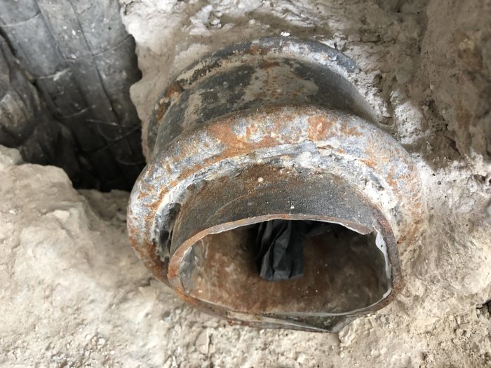 Öppet schakt med ett utskuret gammalt gjutjärnsrör som är framstickande från väggen.
