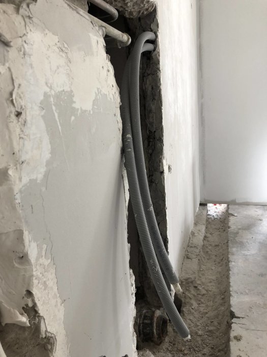 Öppet schakt i vägg med synliga inkommande rör och utgående avlopp under renovering.