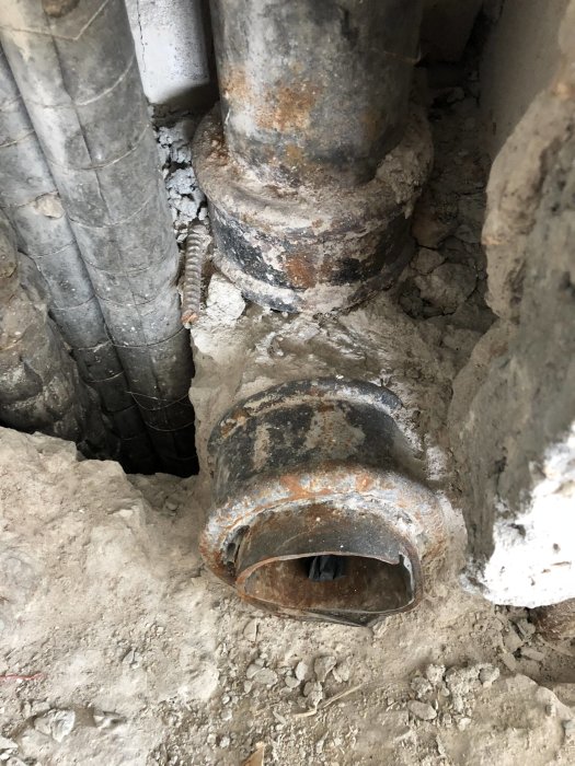 Öppna schakt med synliga, äldre vattenrör och avloppsrör i betonggolv under renovering.