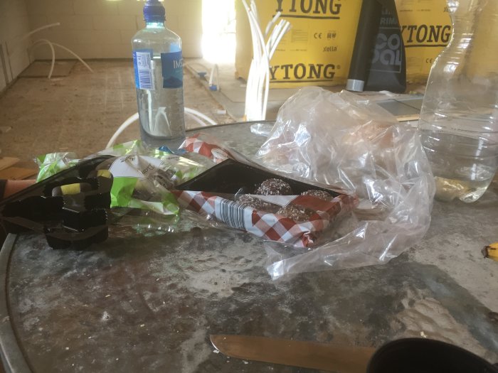 Fikapaus på en byggarbetsplats med öppnad godisförpackning och tomma vattenflaskor på en smutsig byggtunna.