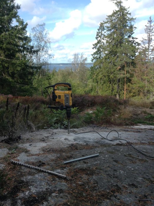 Borrmaskin i bruk utomhus för byggprojekt på en solig dag med skog och himmel i bakgrunden