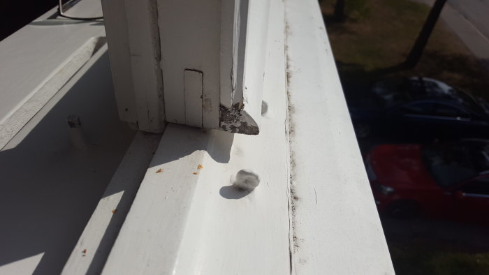 Vit målad fönsterkarm med mystiska öglor på ytan, fönsterdel och bil utomhus synlig.