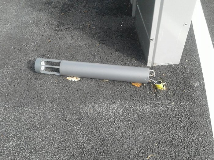 Lampa med 90-graders krokar lossad från asfalten, bredvid en grå fiberskåp.