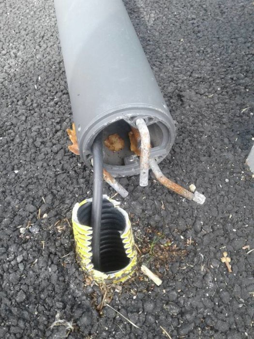 Metallkrokar och kabel inuti en lampa liggande på asfalt, lossnad från dess fäste.