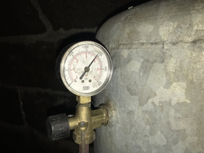 Manometer med tryckmätning på en hydrofor i ett dunkelt utrymme, potentiellt problem med vattentryck.