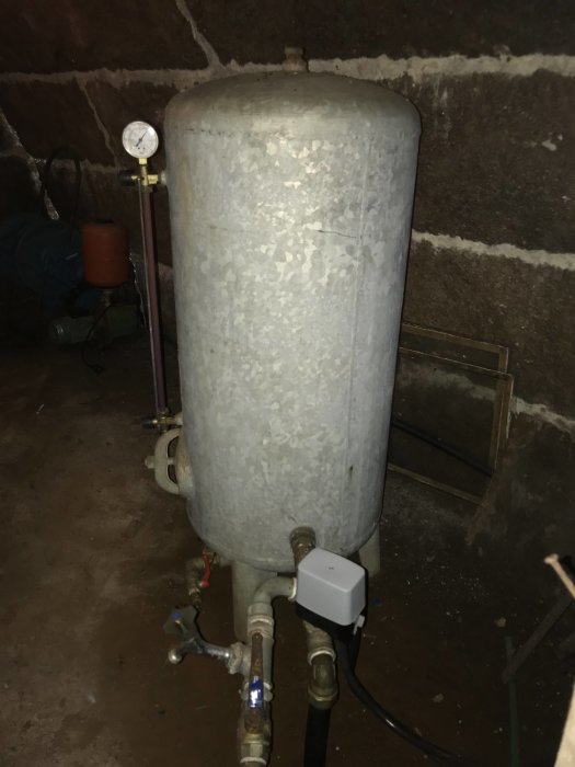 Hydrofor i jordkällare med tryckmätare, rör och strömbrytare.
