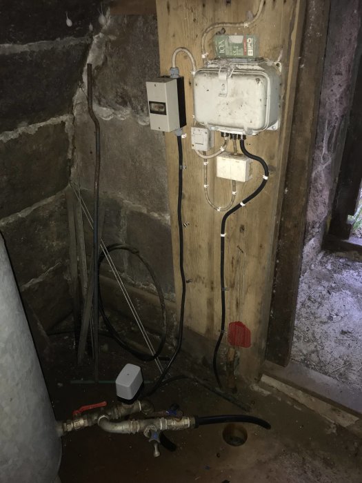 Eldriven utrustning i ett stenrum med hydrofor, ledningar, och elektrisk strömbrytare.