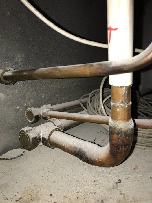 Oavslutade kopparvärmeslingor och avskurna rör utanför en vägg, indikerar ett ofärdigt installationsprojekt.