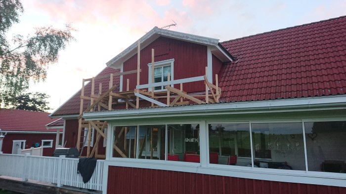 Nyligen målat rött hus med ny vindskiva och byggnadsställning under fönster.