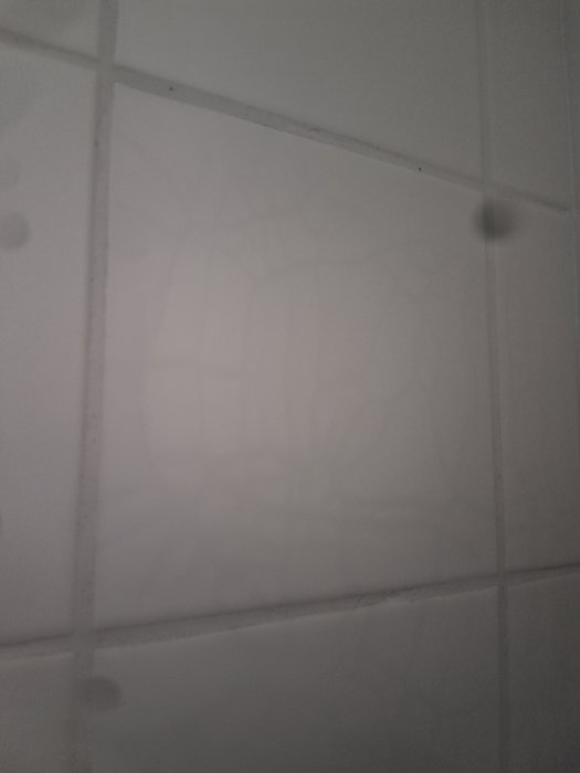 Sprick-liknande missfärgningar på ett vitt kakel i dusch efter användning av rengöringsmedel.