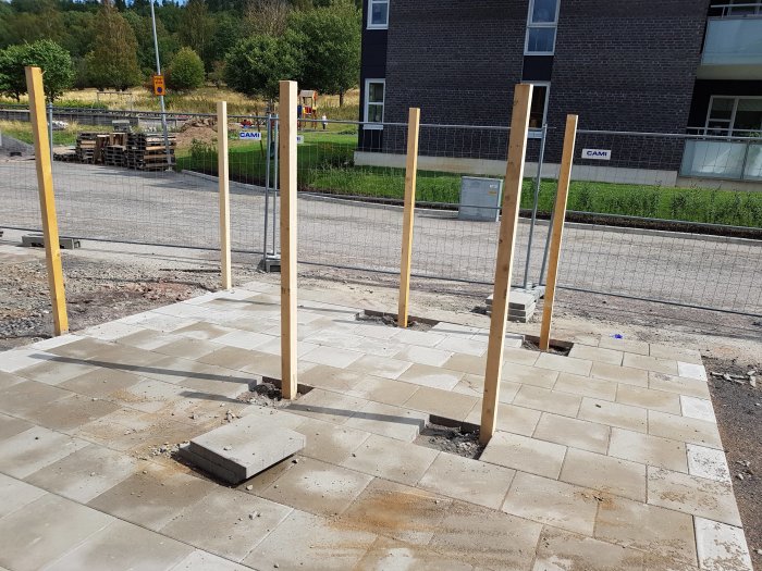 Obehandlade träreglar gjutna i marken vid bygge av staket på framsidan av ett radhus.