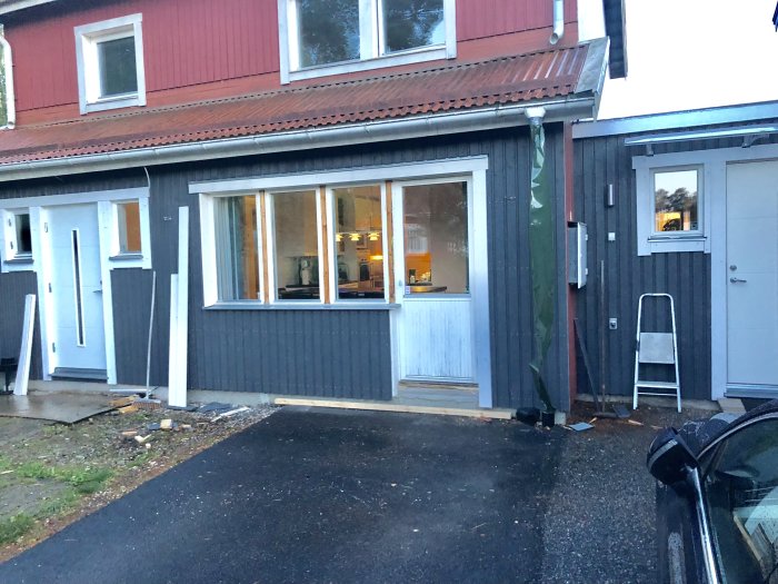 Husfasad under renovering med ny panel och verktyg utspridda på marken.