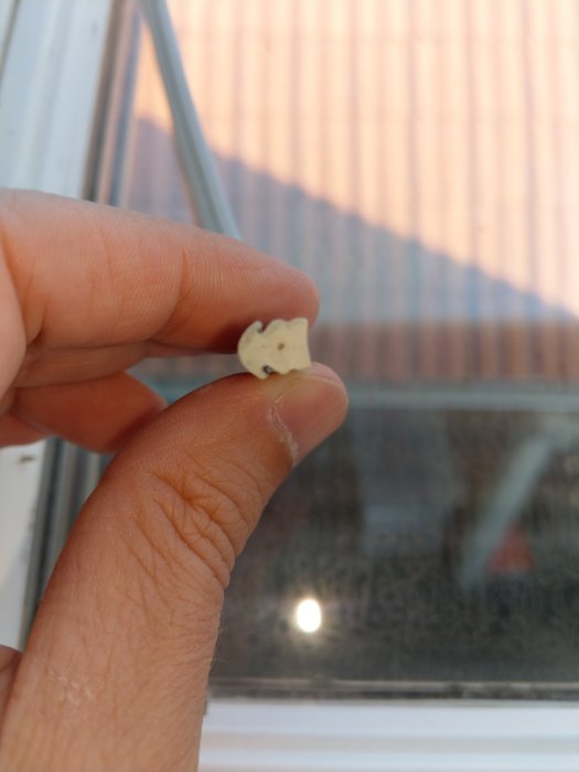 Hand håller en gammal vit tätningslist mot fönster, mäter bredden mellan tumme och pekfinger.