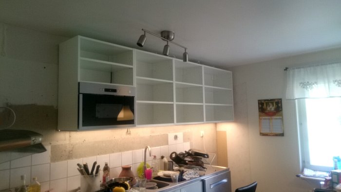 Vit högglansigt skåp med öppen glipa mot taket i ett kök under renovering.