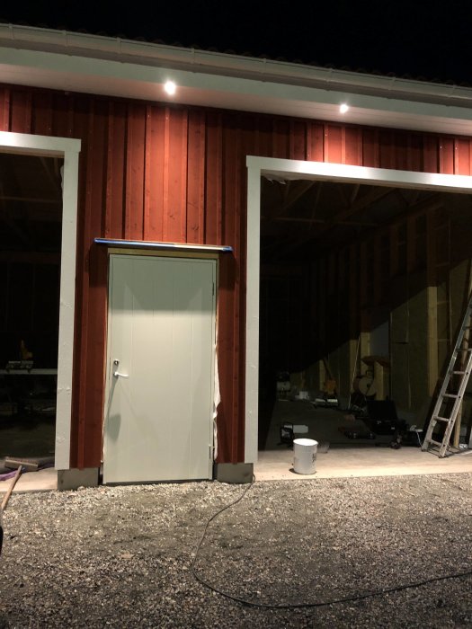 En nyinstallerad vit dörr på en röd trälada vid kvällsbelysning, med byggmaterial synliga inuti.