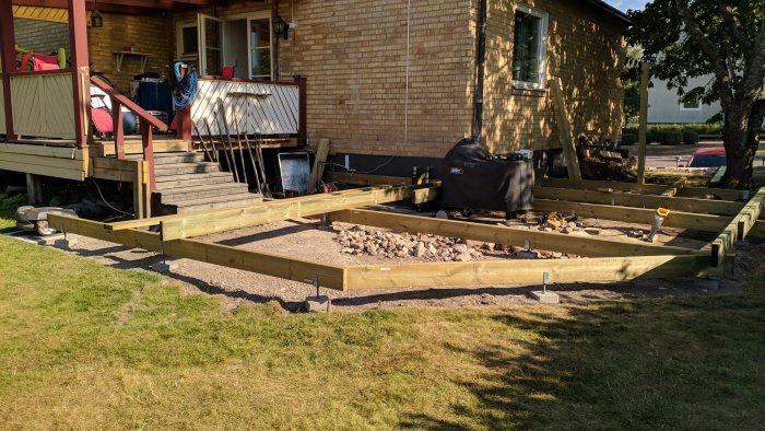 Grundkonstruktion av trädäck under arbete bredvid hus med gammal altandel kvar.