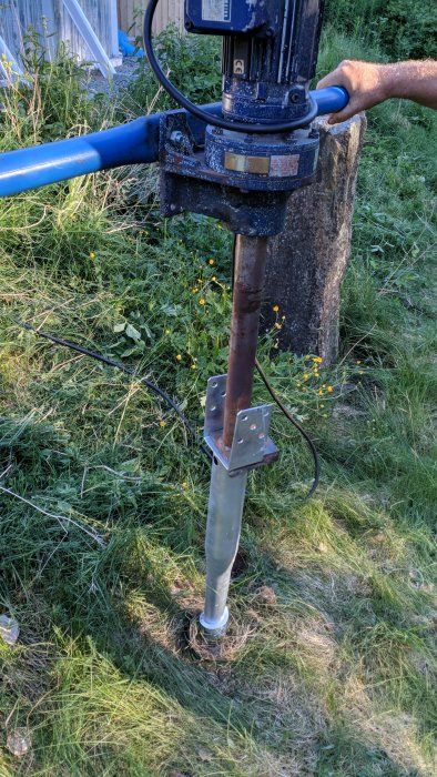 Maskin för installation av markskruv som fäster en markskruv i gräsmarken, med stenig mark som problem.
