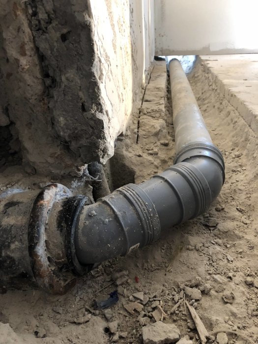 Nyinstallerad avloppsrör ansluten till äldre del i en grusig byggarbetsplats.