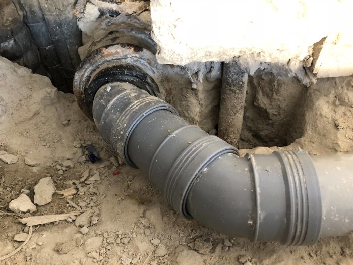 Nyinstallerat avloppsrör i grått plastmaterial som ansluter till gammalt rörsystem i en byggarbetsmiljö.