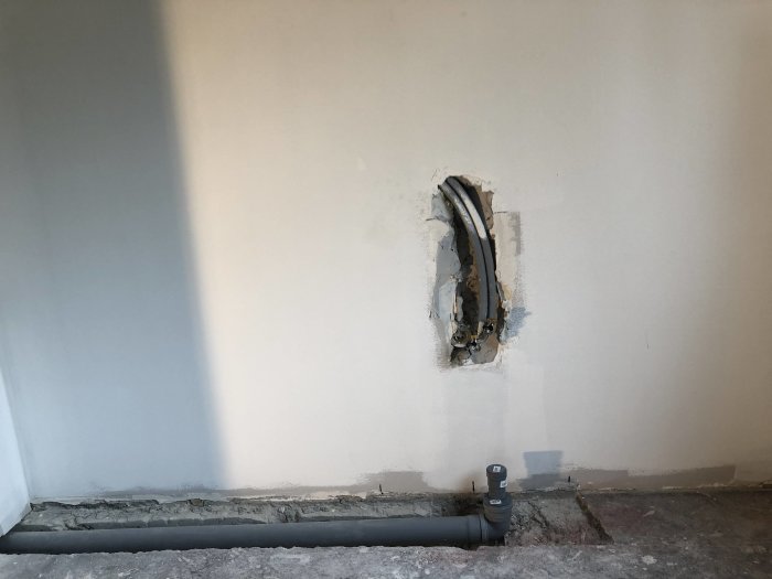 Nyinstallerad avloppsrör i vägg och golv med synligt arbete innan slutspackling och målning.