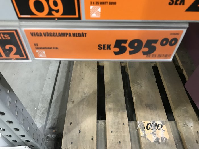 Prisskylt för en Vega vägglampa med prisinformation, över trälattor på golvet i en butik.