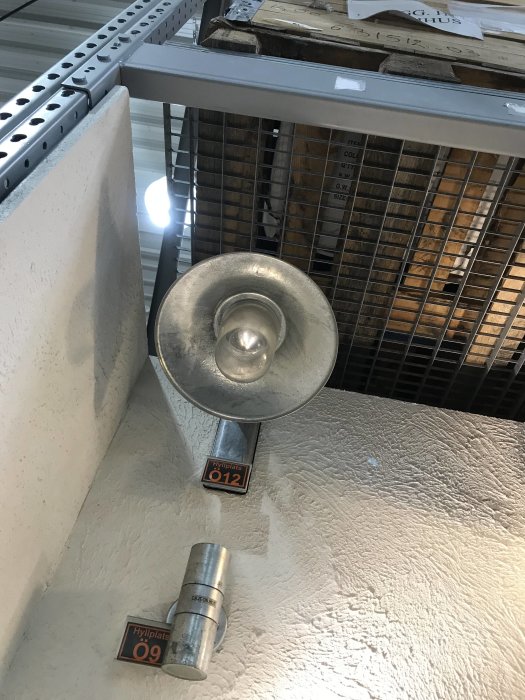 Metallampa monterad på ytterhörn av vit fasad med rektangulär bas och sifferetikett 012.