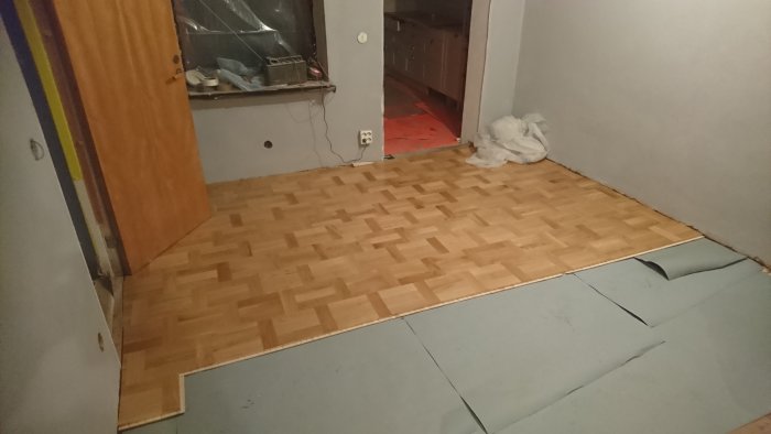 Delvis lagt parkettgolv i ek i holländskt förband ovanpå grålumppapp i ett rum under renovering.