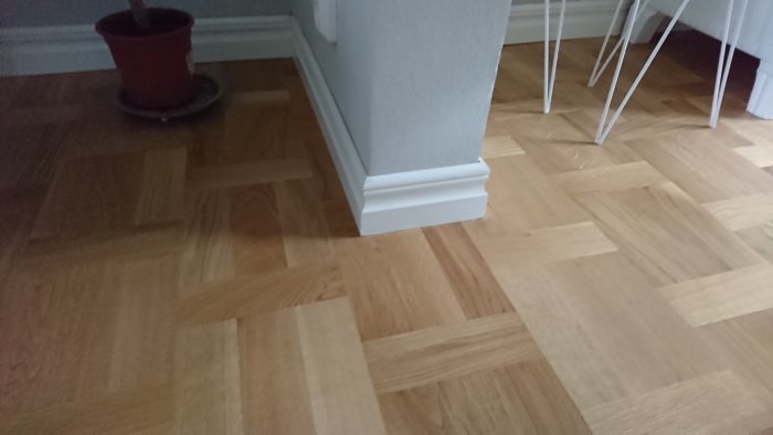 Nyinstallerat ekgolv i holländskt förband med vit sockellist och en del av en växtkruka samt stolsben.