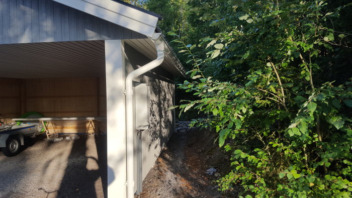 Nyinstallerade hängrännor och stuprör på en carport, omgivna av grönska och solsken.