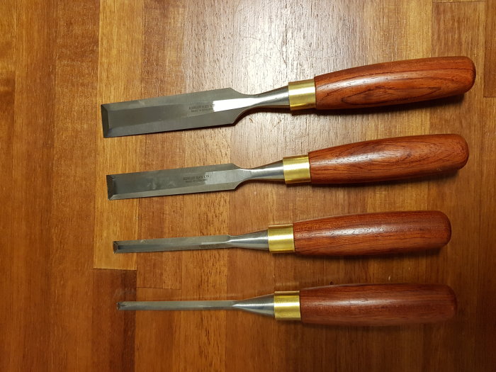 Fyra Ashley Iles stämjärn med olika breda blad och trähandtag ligger på ett träbord.