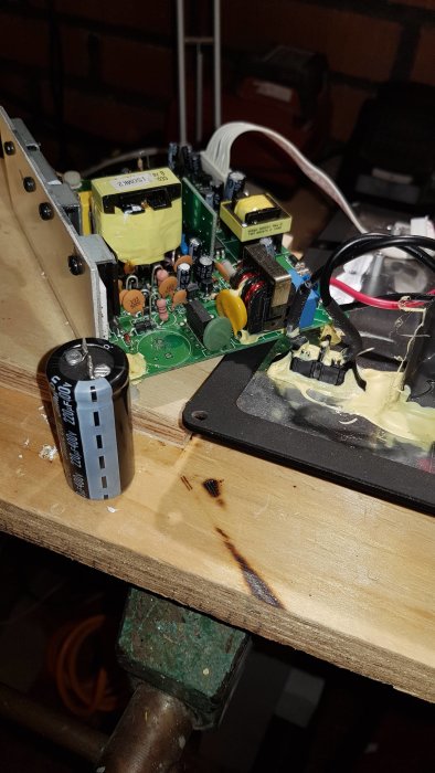 Öppnad subwoofer med ny lödd kondensator och reparerad potentiometer på en träbit i ett garage.