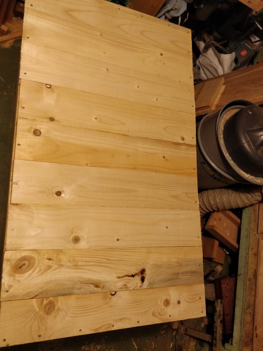 Nybyggt spikat trägolv av plankor i en verkstadsmiljö, med verktyg i bakgrunden.