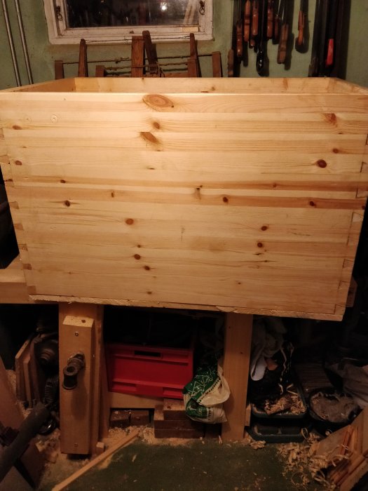 Trälåda under arbete i verkstad med verktyg på hylla i bakgrunden och hyvelbänk delvis synlig.