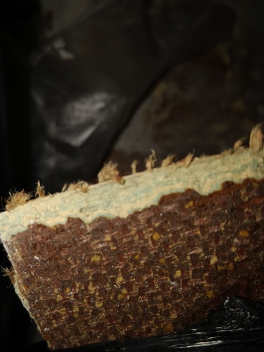 Närbild på ett lager av äldre golvmaterial som kan innehålla asbest, med synliga fibrer och limrester.