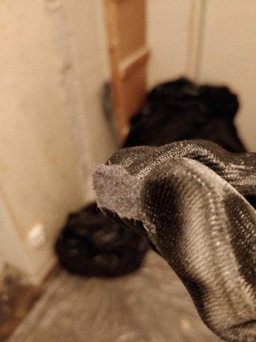 Närbild på en hand som håller i en slingrande kant av en gammal golvmatta under en renovering.