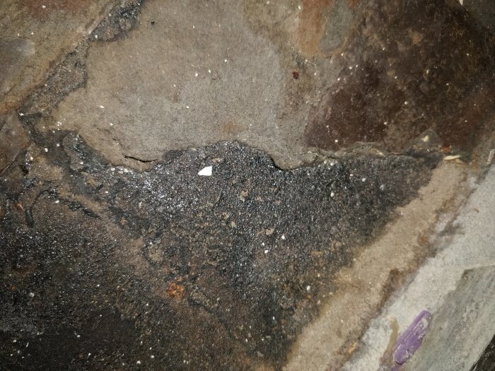 Äldre bottenlager av golv med misstänkt asfaltpapp och rester av svart lim, möjlig asbestexponering under renovering.