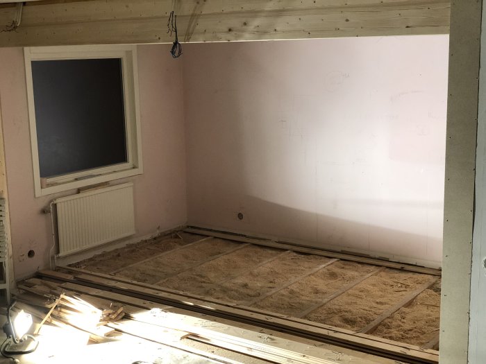 Renoveringsrum med uppbrutet golv, exponerade isoleringsplattor av kutterspån och träreglar.