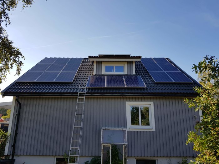 Solpaneler installerade på ett hus med lutande tak och en stege lutad mot husväggen.