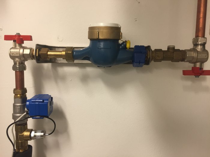 Vattenmätarinstallation med plomberad mässingring och rörsystem på vägg.