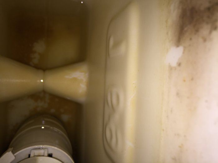 Inuti en inbyggd WC-cistern med synliga vattenavlagringar och inga tydliga varumärkesmärken.