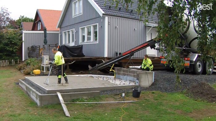 Nygjuten och glättad betongplatta med arbetare och betongbil på en byggarbetsplats.