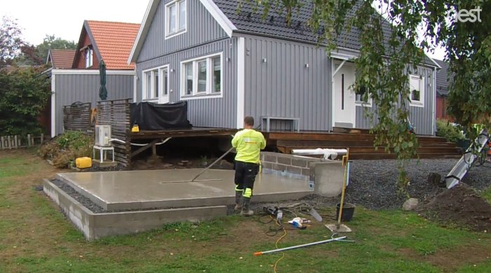 Arbetare i hög synlighetkläder glättar en nyligen gjuten betongplatta vid ett hus.