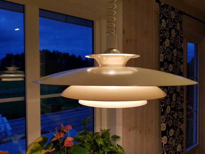 Kökslampa med unik design tänd inomhus framför ett fönster i skymning, inte ett UFO utanför.