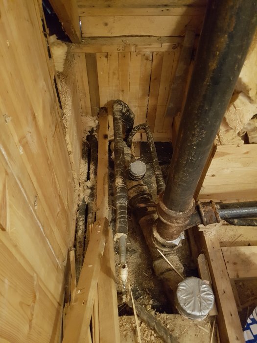 Renovering av badrum med öppet golv och exponerade gamla rörledningar i ett träkonstruktionsschakt.