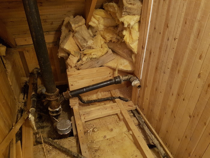 Renoveringsprojekt av toalett med synliga rör och väggar i trä, schakt för stambyte.