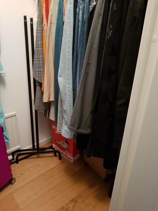 Walk-in closet med hängande kläder och en skohylla, söker förslag för bättre utrymmesanvändning.